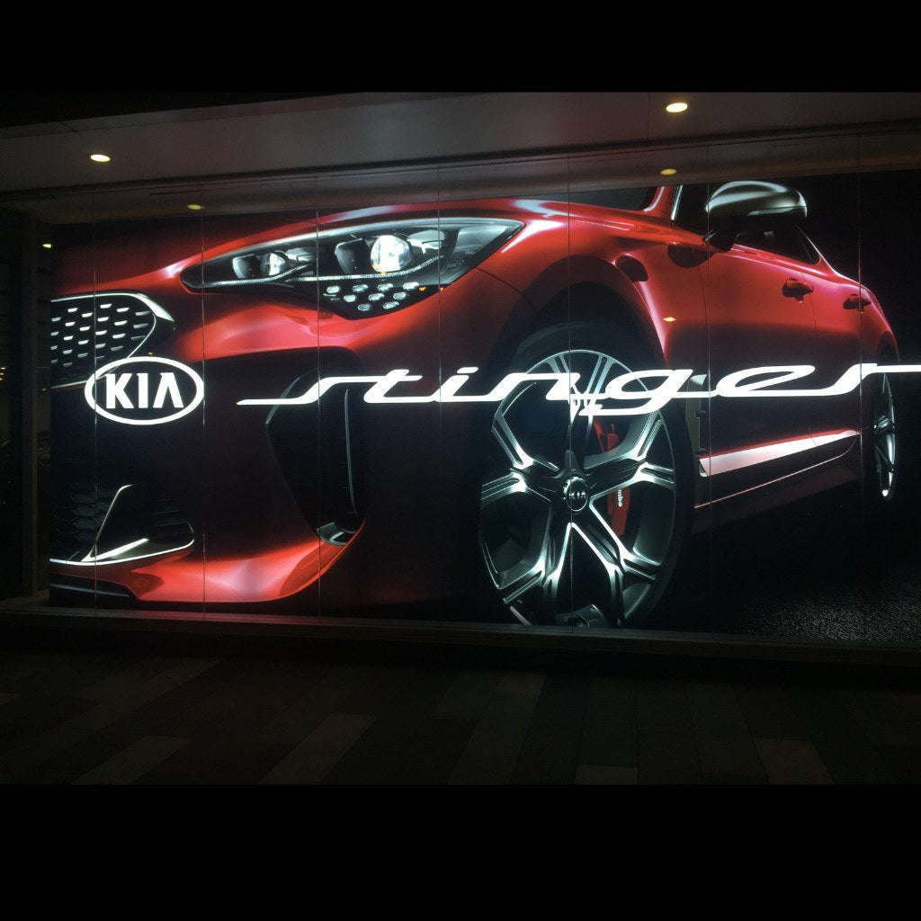 Backlit Kia Stinger lightbox display reading through the showroom glazing at night