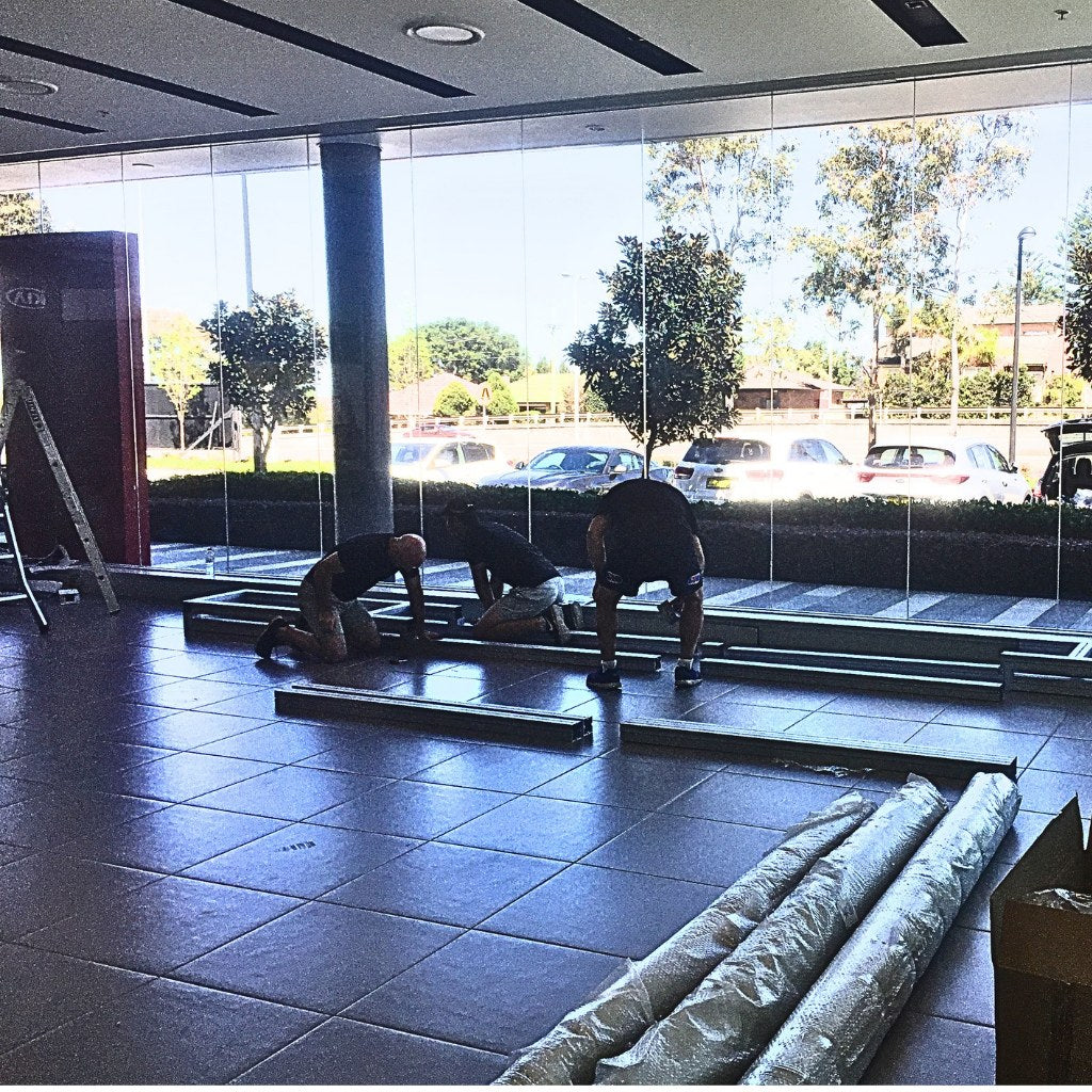 Installation crew assembling numbered lightbox frame segments on the cleared showroom floor, Kia Australia head office